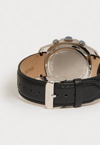 Ρολόι χειρός με ασημί απόχρωση και μπλε λεπτομέρειες, μαύρη δερμάτινη λωρίδα, γυαλιστερό κουτί και λείο στρογγυλό πίσω μέρος. Χαραγμένο κείμενο στο πίσω μέρος του κουτιού.