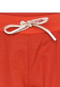Czerwone szorty wykonane z oddychającego materiału mają elastyczny pasek w talii z kontrastowym sznurkiem oraz boczne kieszenie.