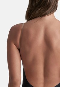 Costume da bagno nero con un profondo scollo sulla schiena, sottili spalline color carne e una texture liscia, che mette in risalto i contorni della schiena e delle spalle.