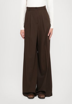 Pantalons à jambes larges en tissu marron foncé, avec une taille haute, des plis et une fermeture à bouton. Assortis avec des chaussures marron.
