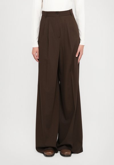 Pantaloni a gamba larga in tessuto marrone scuro, con vita alta, pieghe e chiusura con bottone. Abbinati a scarpe marroni.