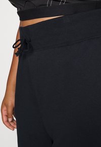 Svart svettbyxor med en bred, ribbad midja och dragsko-stängning. Slät tygtextur. Synlig sömdetalj på sidan.