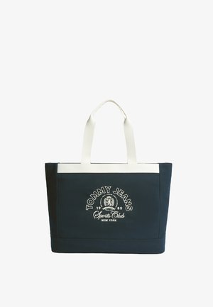 Borsa tote blu navy con manici bianchi, bordo superiore bianco e logo bianco "Tommy Jeans Sports Club New York 1985" sul davanti.
