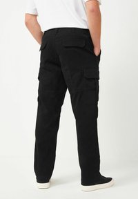 Schwarze Cargo-Hosen mit entspannter Passform, ausgestattet mit mehreren Seitentaschen und einem strapazierfähigen Stoff. Getragen mit einem weißen Shirt und schwarzen Sneakers.