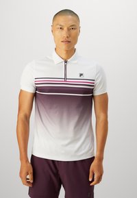 Homme portant un polo blanc et violet en dégradé avec des rayures et un short violet assorti, se tenant devant un fond clair uni.