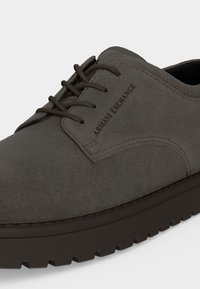 Γκρι καστόρινο παπούτσι Armani Exchange με κορδόνια, χοντρή μαύρη σόλα και εμφανές όνομα μάρκας στο πλάι.