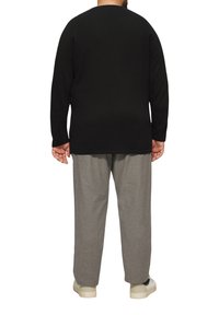 Zwarte lange mouwen shirt, casual fit, gecombineerd met lichtgrijze op maat gemaakte broek. Witte sneakers maken de outfit compleet. Effen achtergrond.