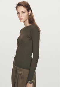 Oliwkowy, prążkowany top z długim rękawem i zaokrąglonym dekoltem. W połączeniu z spodniami khaki z wysokim stanem. Prosty design. Gładka tekstura.