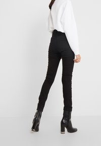 Jeans skinny negros de talle alto con una textura suave, presentan una pierna afinada y costuras sutiles, combinados con botines negros de tacón.