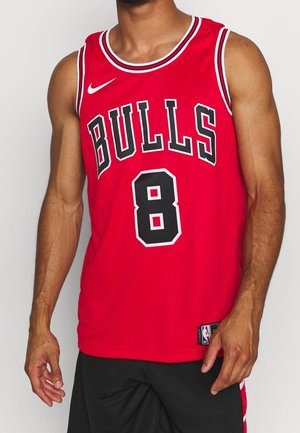 Mężczyzna w czerwonej koszulce koszykarskiej Chicago Bulls bez rękawów z numerem 8 i czarnych sportowych szortach na jednolitym tle.