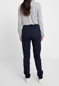 Granatowe spodnie o gładkiej fakturze, dopasowanym kroju i tylnych kieszeniach. Połączone z białą, wzorzystą koszulą z długim rękawem i białymi trampkami.