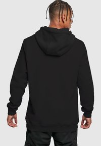 Čierna mikina s klokankou, s kapucňou na šnúrky a ribbenými manžetami. Tkanina vyzerá mäkko a textúrovane, ideálna na neformálne nosenie.