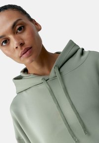 Felpa verde chiaro caratterizzata da un cappuccio spesso con coulisse, texture liscia e dettagli minimali nelle cuciture. Adatta per un abbigliamento casual o come strato da indossare.