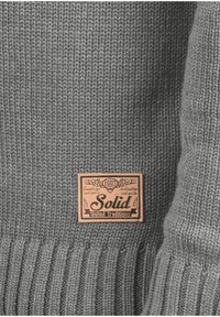 Grijs gebreid sweater met een geribbelde zoom en een textuur oppervlak. Voorzien van een tan leren label met het opschrift "Solid United Traditions".
