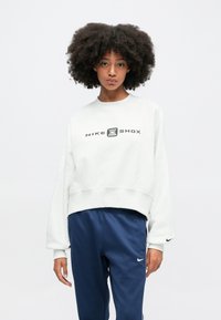 Svetlo šedý krátky sveter s čiernym logom "NIKE SHOX", v kombinácii s tmavomodrými nohavicami so malým logom Nike. Mäkko, textúrované tkanivo.