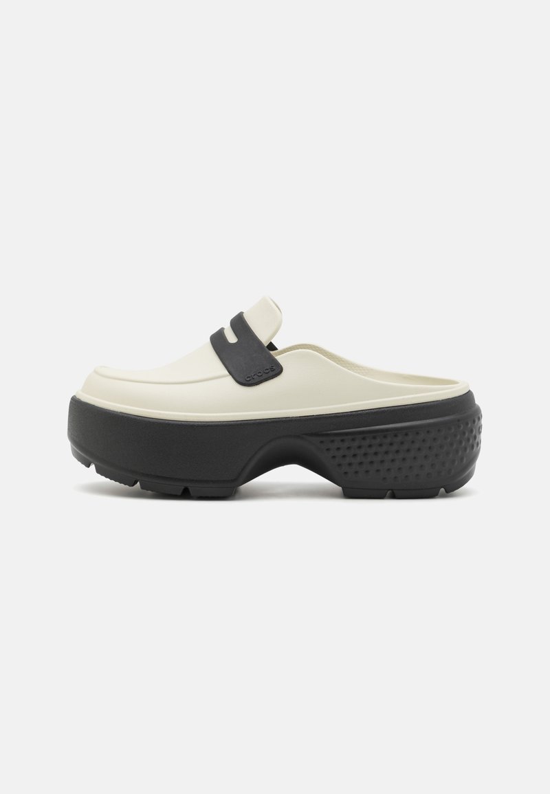 Chaussure slip-on crème avec une épaisse semelle plateforme noire et un détail de bride noire sur le dessus, vue de côté sur fond blanc.