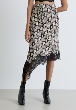 Femme portant une jupe asymétrique à imprimé serpent avec bordure en dentelle noire et bottines noires, debout avec une main le long du corps.
