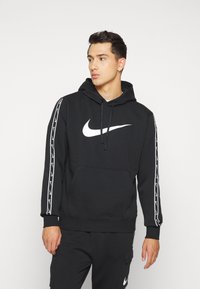 Felpa nera con cappuccio realizzata in tessuto morbido, caratterizzata da un grande logo Nike bianco sul davanti e strisce di branding bianche sulle maniche.