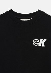 Black sweatshirt with ribbed round neckline, featuring a white "CK" logo on the left chest. Made from soft, smooth fabric.