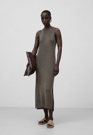 Robe en tricot, sans manches, en bronze avec des fentes sur les côtés, associée à une pochette marron et des sandales beiges, sur un fond uni. Texture lisse et coupe ajustée.
