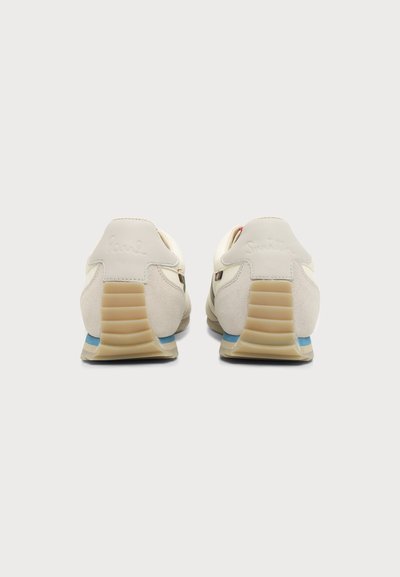 Paire de baskets blanc cassé avec talons côtelés beige et accents bleus vues de dos sur un fond gris clair uni.