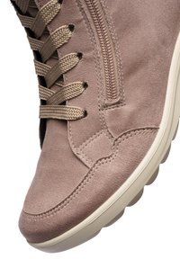 Zapatilla de ante marrón claro con cordones beige, cremallera lateral, costuras detalladas y suela blanca con estrías.