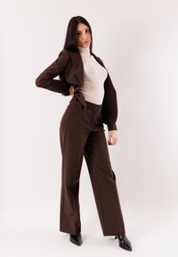 Completo marrone su misura con pantaloni a gamba larga e dolcevita bianco aderente. Scarpe nere con tacco alto. Tessuto liscio, design blazer strutturato.