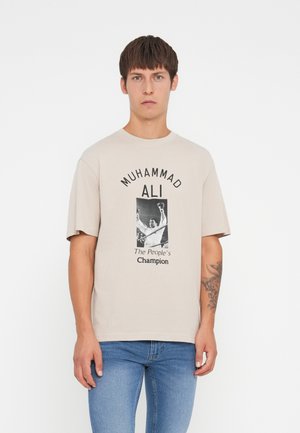 Beige Baumwoll-T-Shirt mit einer schwarz-weißen Grafik eines Boxers und dem Text "MUHAMMAD ALI The People's Champion." Lockerer Schnitt, kurze Ärmel.