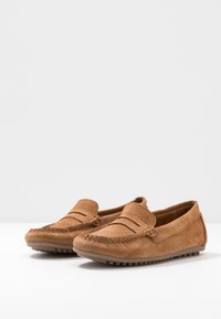 Mocassins en suède marron avec un détail de couture et une semelle en caoutchouc. Le design présente une coupe basse et une texture douce.
