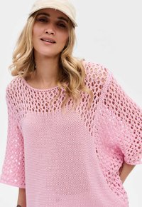 Lichtroze gebreide top met een losse, open breiselontwerp, korte mouwen en een ronde halslijn. Zachte textuur, casual stijl.