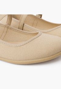 Bailarinas de lienzo beige con parte superior texturizada, punta cerrada y correa ajustable. Suela de goma plana para mayor comodidad y estabilidad.