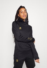 Zwarte sportieve pullover met hoge kraag, gouden logo en accenten. Voorzien van lange mouwen en een relaxed fit, gemaakt van een gladde, ademende stof.