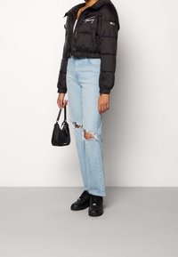 Černá puffer bunda s zkráceným střihem a kapucí, světle modré roztrhané džíny a černé tenisky. Malá černá kabelka s krátkým popruhem.