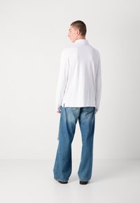 Hvit langermet skjorte med stående krage, båret med løse, lyseblå denimjeans, med en litt slitt nederkant og侧 slisser.