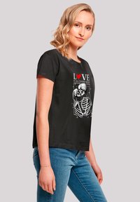 Black cotton t-shirt featuring a skeleton design with red heart and white text. Short sleeves, relaxed fit, and crew neckline.
