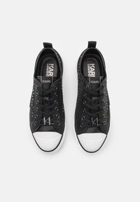 Schwarzer Sneaker mit einer strukturierten Oberseite, auffälliger Schnürung, Gummispitze und einem Logozug. Glatte Seitenpaneele und weiße Sohle.