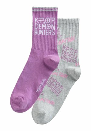 Üks lilla sokk, millel on valgete tähtedega kiri "KPOP DEMON HUNTERS", ja üks hall sokk, millel on roosad tähed ning korduvad "KPOP DEMON HUNTERS" mustrid.