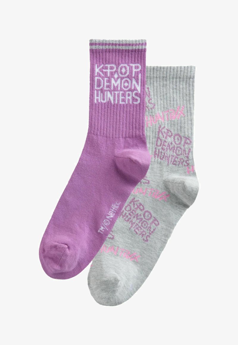 Un șosetă mov cu textul „KPOP DEMON HUNTERS” scris alb și o șosetă gri cu text roz și modele repetate „KPOP DEMON HUNTERS”.