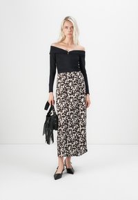 Off-the-shoulder svart topp med rynker; lang mønstret skjørt i mørkebrunt og krem; svart veske med frynser; spisse svarte hæler.