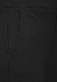Pantalons de jogging noirs présentant une texture lisse, une taille élastique et des poches latérales. Le tissu est léger et légèrement extensible.