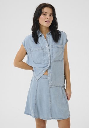 Outfit in denim azzurro chiaro con una camicia a maniche corte con bottoni e due tasche frontali, abbinata a una gonna, entrambi con dettagli di cucitura sottili.