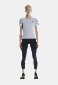 Helles blaues Sport-T-Shirt mit kurzen Ärmeln und Logo auf der Brust, kombiniert mit marineblauen Leggings. Das Model trägt schwarze Laufschuhe.
