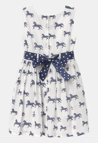 Vitt ärmlöst klänning med marinblå prickig hästtryck och matchande marinblå prickig bälte knutet i en rosett i midjan.