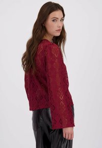 Lace blouse in bordeaux met lange mouwen, een opengewerkt geometrisch patroon en een relaxte fit. Draag het met slanke zwarte leren broek.
