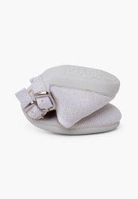 Chaussons en tissu blanc avec un dessus texturé, dotés de deux boucles en métal argenté et d'une semelle en caoutchouc arrondie. Design compact et pliable.