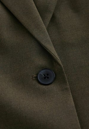 Dark olive green fabric with a single large black four-hole button fastening a tailored garment's lapel.
