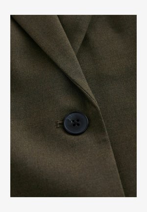 Țesătură verde măsliniu închis cu un singur nasture mare negru cu patru găuri care fixează reverul unui articol de îmbrăcăminte croită.