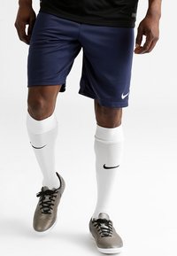 Navy athletic shorts with a smooth texture and Nike logo, paired with knee-high white socks featuring a black Nike swoosh and grey soccer shoes.