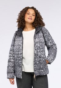 Giacca grigia trapuntata con motivo a zigzag, colletto alto e cappuccio nero. Include una cerniera frontale e tasche laterali.