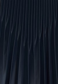 Marinblå, plisserad tyg med vertikala veck, som har en slät yta och glans. Vecken är jämnt fördelade och definierade.